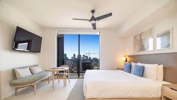 A modern hotel room with a large bed, a flat-screen TV mounted on the wall, a balcony with a city view, and a ceiling fan. - Modern Studio with Balcony in Downtown Miami (Miami)