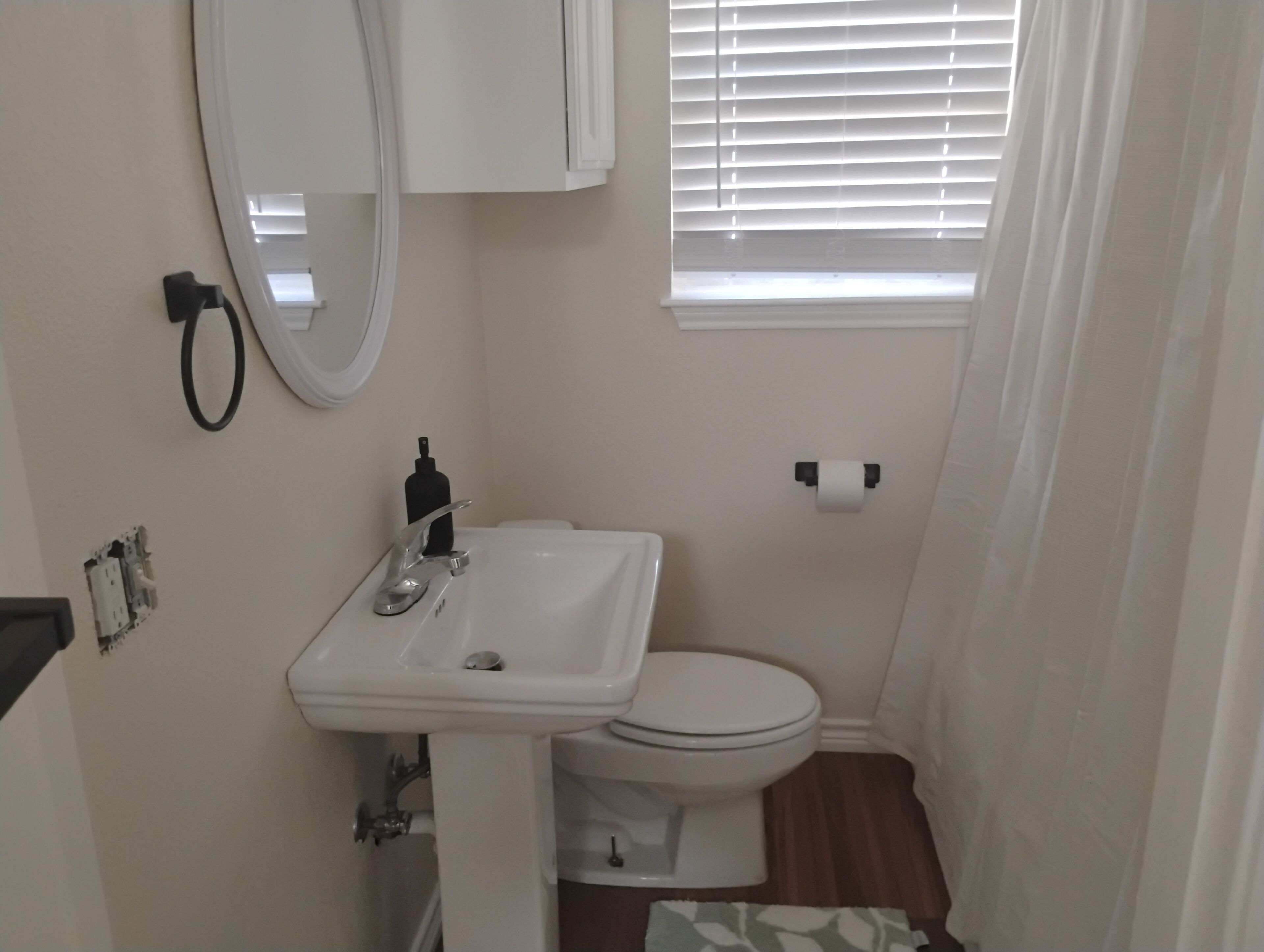 Une petite salle de bain avec un lavabo blanc, des toilettes et une fenêtre avec des stores.