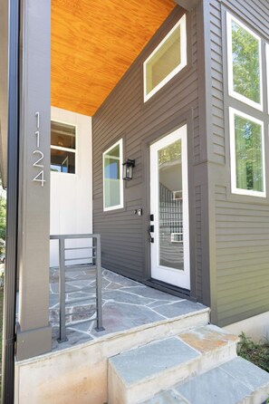 A modern house with a stone-paved entrance, a wooden ceiling, and a number '1124' on the wall. - 8 Min to Duke + Downtown | Back Deck (Durham)