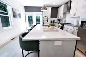 A modern kitchen with a central island, white cabinetry, and a view to the outdoors. - 8 Min to Duke + Downtown | Back Deck (Durham)