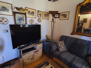 A living room with a flat-screen TV, a sofa, a coffee table, and various framed pictures on the wall.