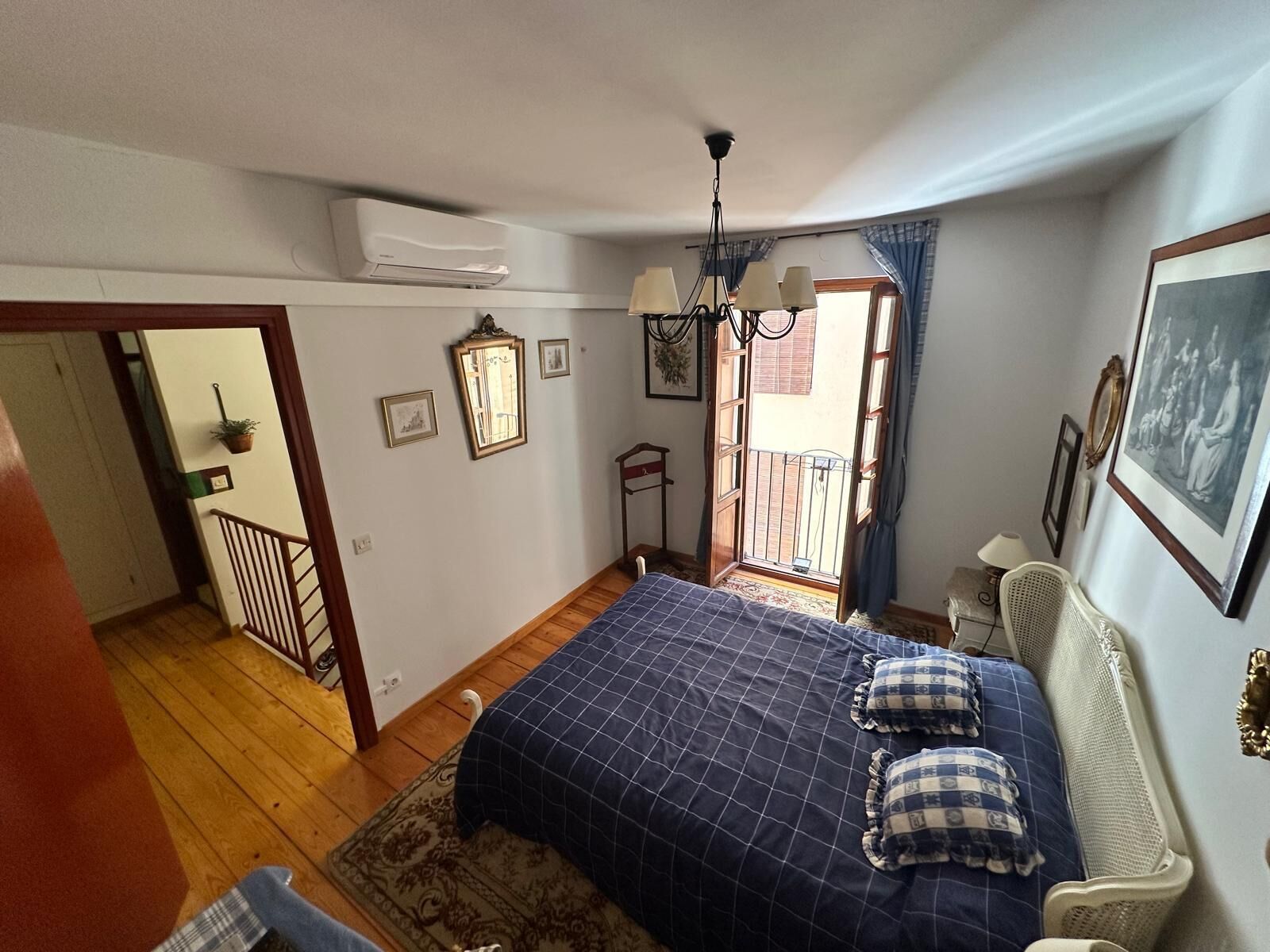 A bedroom with a bed, a chair, a window, and a door leading to a balcony.