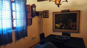 A dining area with a table, chairs, a wall-mounted clock, and a framed still life painting.