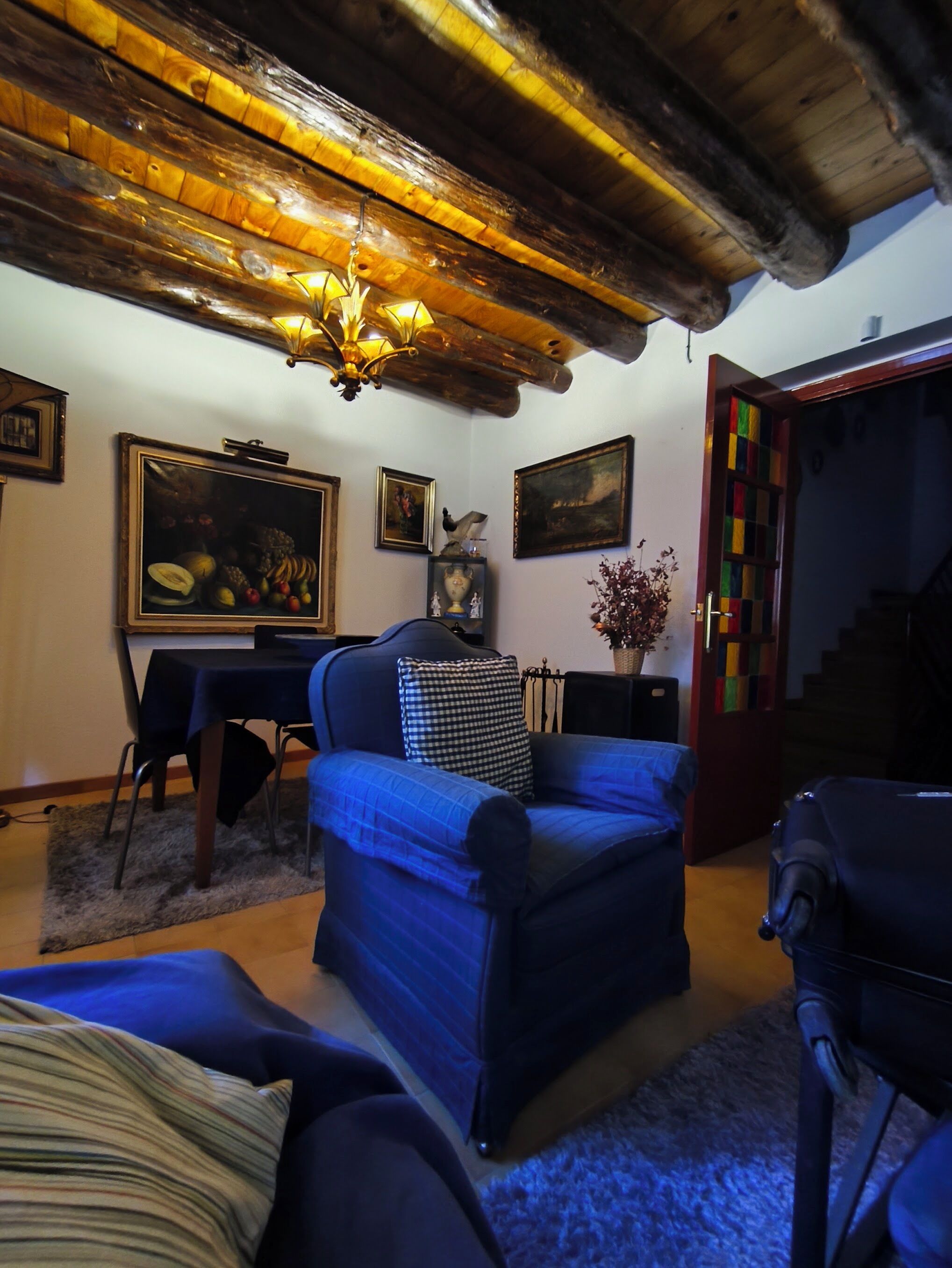 Una habitació amb un sofà blau, una taula de dinar amb caires, una làmpada penjant i una escala amb una porta colorida.