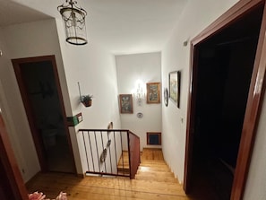 A wooden staircase leading to a landing with a chandelier, framed artwork, and a potted plant.