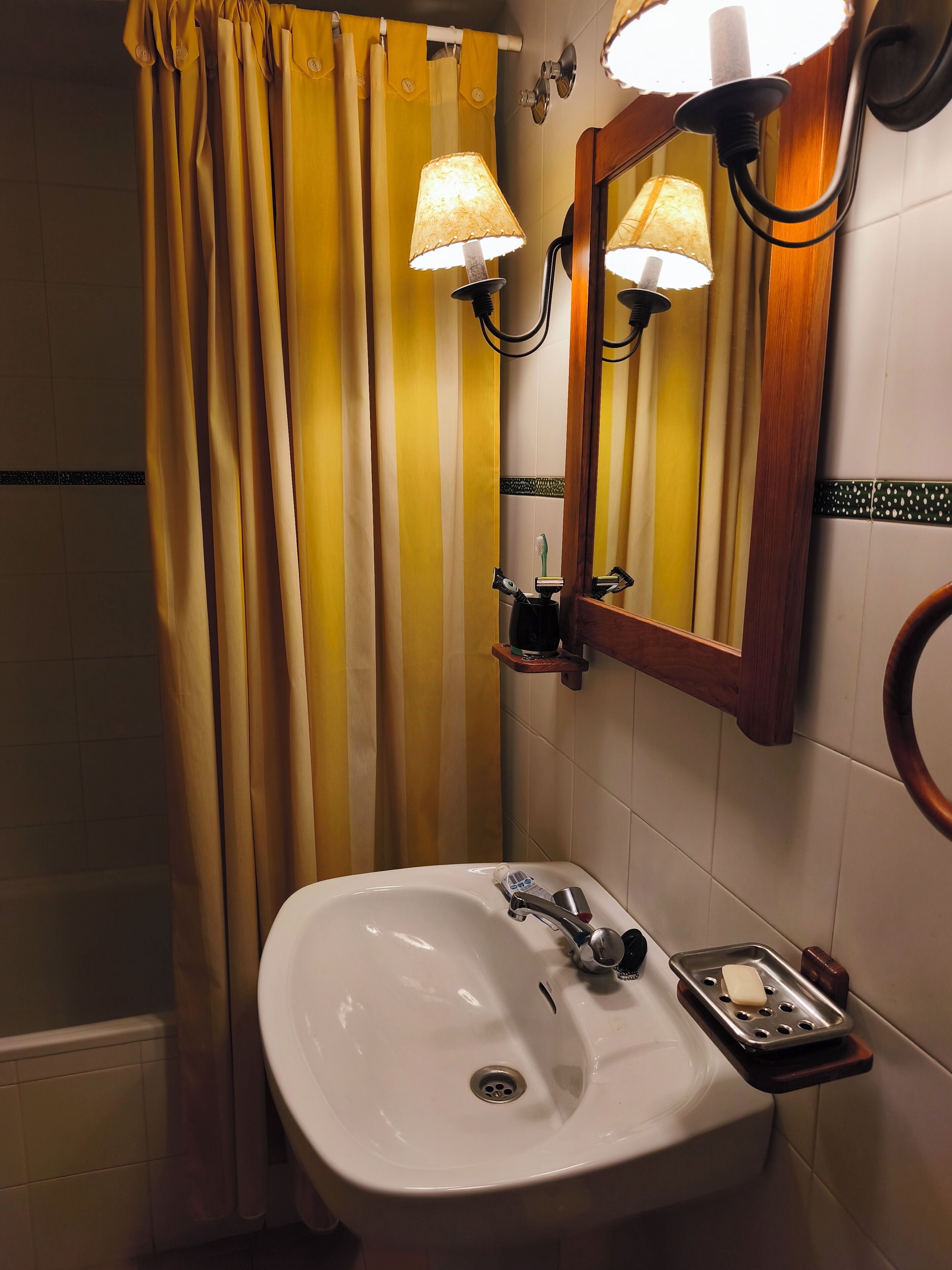Un bany amb un lavabo blanc, un mirall i cortines grogues.