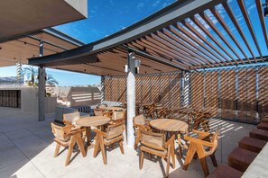 Un espace extérieur aménagé avec des tables et des chaises en bois, une structure en forme de pergola et une vue sur le ciel.