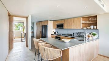 A modern kitchen with wooden cabinets, a central island with bar stools, a built-in microwave, and a stainless steel refrigerator.