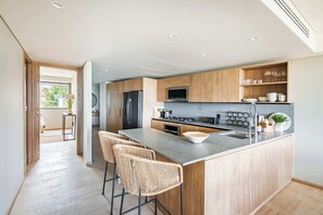 Une cuisine moderne avec des meubles en bois, un îlot central doté de tabourets de bar, un four à micro-ondes encastré et un réfrigérateur en acier inoxydable.