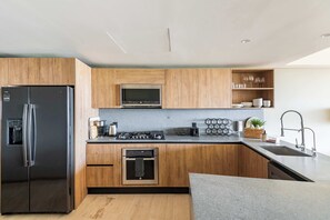 A modern kitchen with wooden cabinets, stainless steel appliances, and a built-in microwave. - Rooftop Infinity Pool & Ocean Views (San José del Cabo)