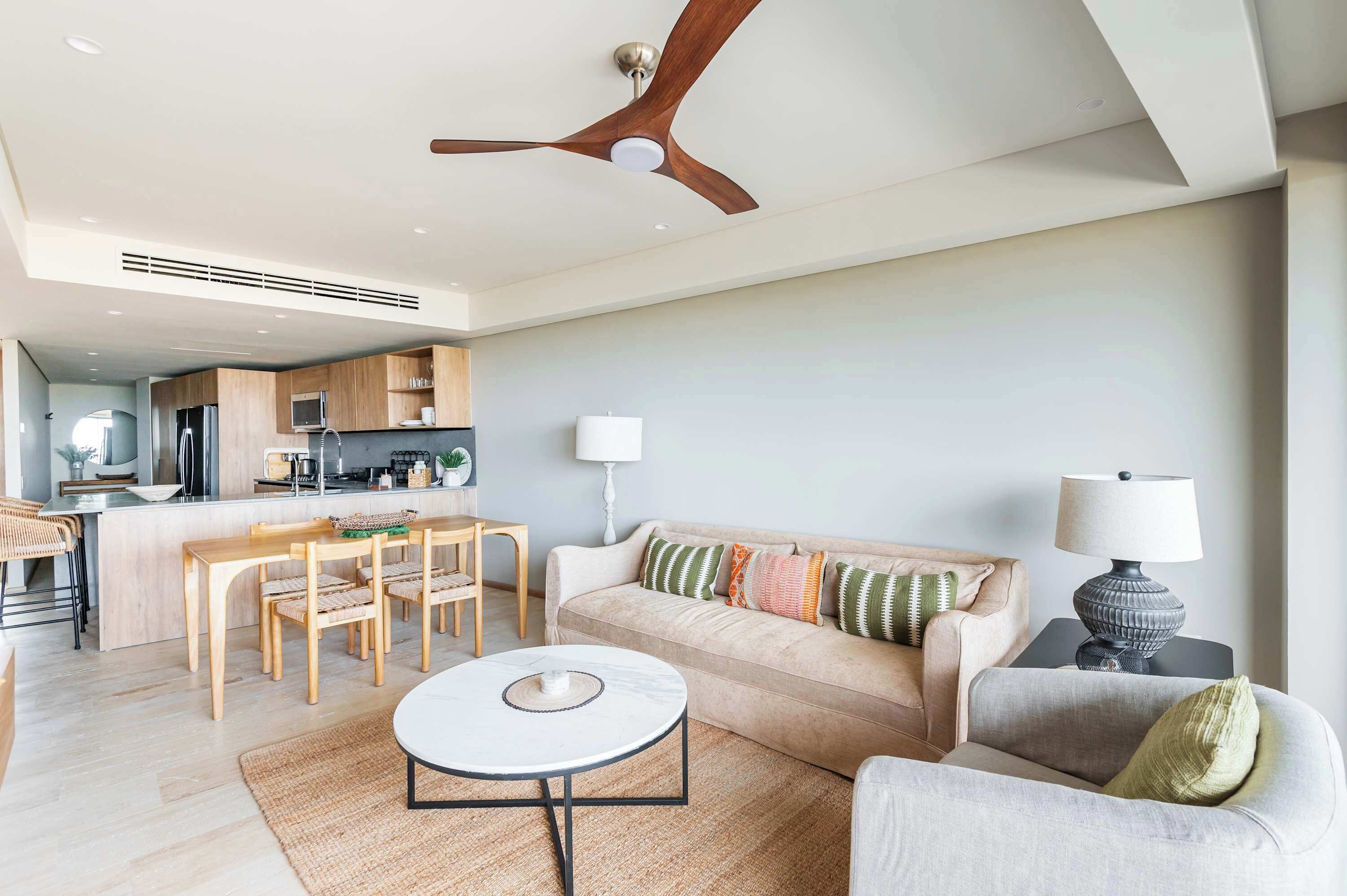 A modern living room with a sofa, a dining table, and a coffee table. There is a kitchen area with cabinets and a microwave.