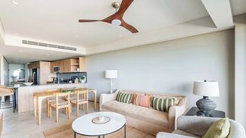 A modern living room with a sofa, a dining table, and a coffee table. There is a kitchen area with cabinets and a microwave.