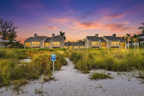 A beachfront property with multiple buildings, a sandy path leading to the entrance, and a sign indicating a beach access point. - Sunset at Banyan Bay|Gulf-Front Condo on Longboat Key Beach+Pool+Tennis |Sleep 8 (Longboat Key)
