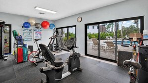 Een sportschool met fitnessapparatuur, een wandklok en uitzicht op een zwembad door grote ramen.