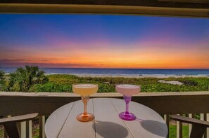 Ein Tisch mit zwei Gläsern mit einem Getränk, mit Blick auf einen Strand bei Sonnenuntergang.