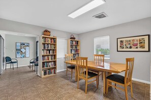 A dining area with a wooden table and chairs, surrounded by bookshelves filled with books. - Sunset at Banyan Bay|Gulf-Front Condo on Longboat Key Beach+Pool+Tennis |Sleep 8 (Longboat Key)