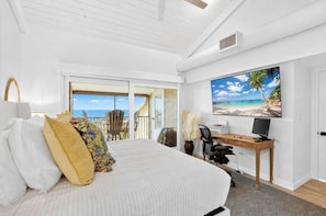 A bedroom with a bed, a desk, a computer, and a large window with a view of the beach. - Sunset at Banyan Bay|Gulf-Front Condo on Longboat Key Beach+Pool+Tennis |Sleep 8 (Longboat Key)