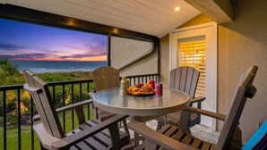 Een balkon met een ronde tafel en stoelen, met uitzicht op een zonsondergang.