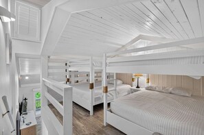 Une chambre avec des lits superposés à plusieurs niveaux, dotée de poutres en bois peintes en blanc et d’un plafond en pente.
