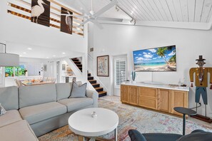 Un salon moderne avec un canapé, une table basse ronde, un téléviseur et un escalier.