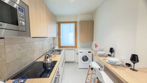 A modern kitchen with a microwave, stove, washing machine, and a window providing natural light. - Velvet Suite by Ca-Sa Check (Chioggia)