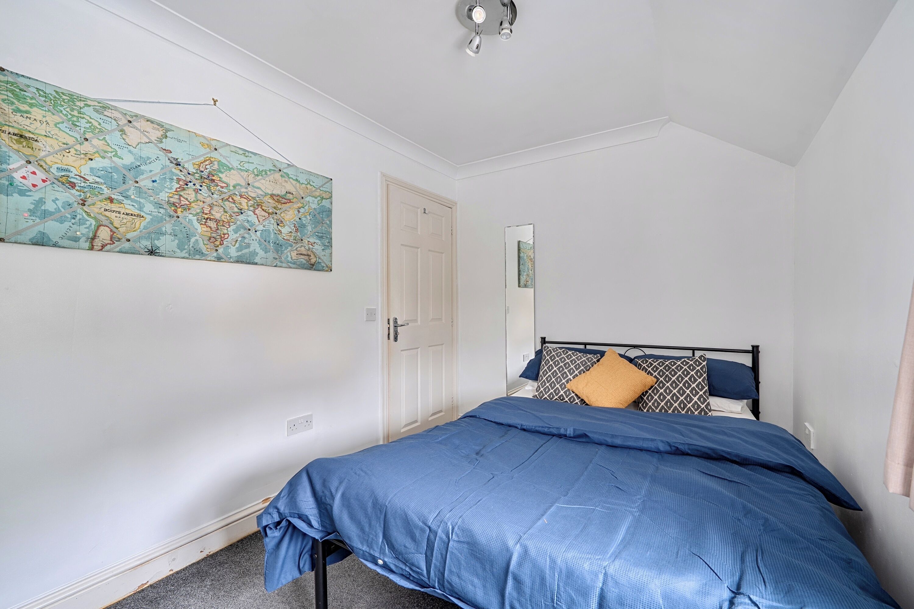 A bedroom with a bed, a map on the wall, a door, and a mirror.