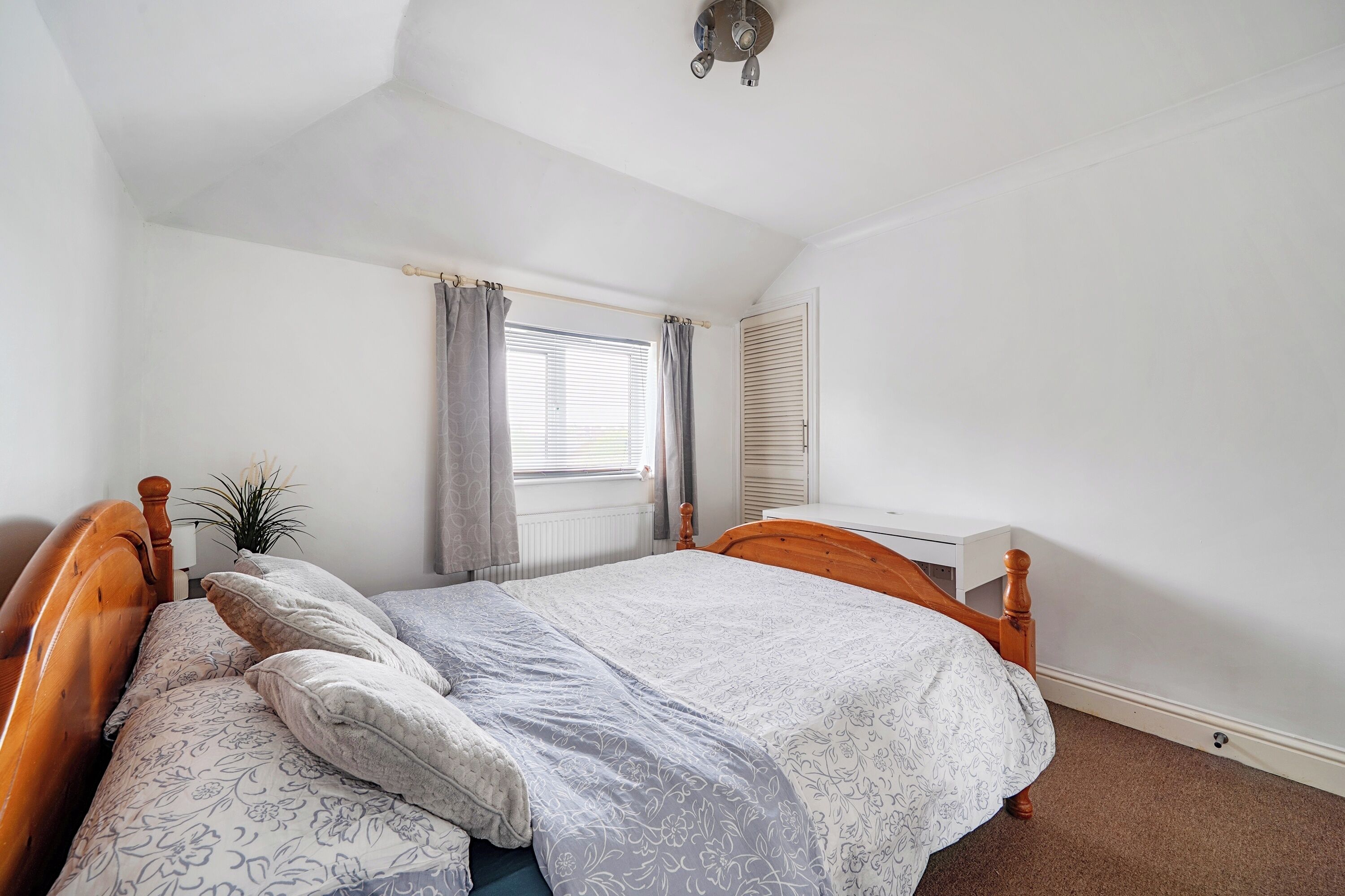 A bedroom with a single bed, a bedside table, a radiator, a window with curtains, and a ceiling fan.
