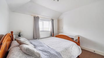 A bedroom with a single bed, a bedside table, a radiator, a window with curtains, and a ceiling fan.