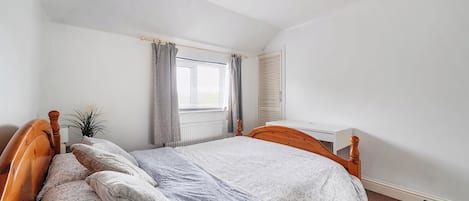 A bedroom with a single bed, a bedside table, a radiator, a window with curtains, and a ceiling fan.
