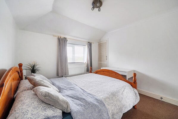A bedroom with a single bed, a bedside table, a radiator, a window with curtains, and a ceiling fan.