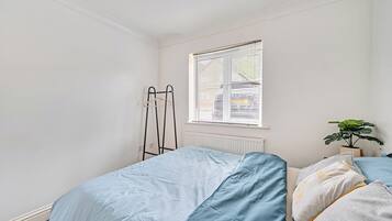 A bedroom with a bed, a radiator, a window with blinds, and a potted plant.