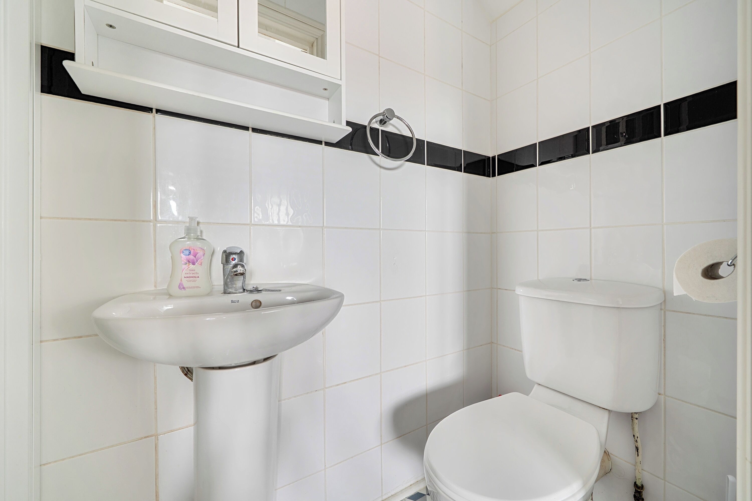 Une salle de bain avec un lavabo blanc, des toilettes et une étagère au-dessus du lavabo.