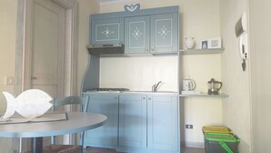 A compact kitchen with blue cabinets, a gas stove, a sink, and a small dining table with a chair. - Ginestre Smeraldo by Casa Check (Porto Rotondo)