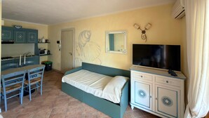 A bedroom with a bed, a TV, a desk with a chair, and a kitchenette. - Ginestre Smeraldo by Casa Check (Porto Rotondo)