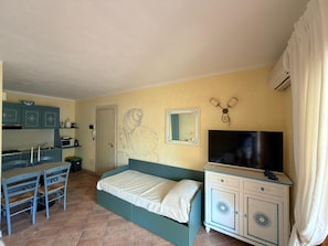 Ein Schlafzimmer mit einem Bett, einem Fernseher, einem Schreibtisch mit Stuhl und einer Küchenzeile.