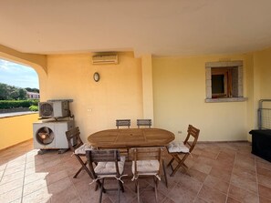 An outdoor patio with a round wooden table and chairs, air conditioning units, and a window with a stone frame. - Mirto Smeraldo by Casa Check (Porto Rotondo)