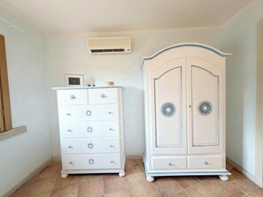 A room with a white dresser with drawers and a decorative panel, a white wardrobe with a circular design, and an air conditioning unit on the wall. - Mirto Smeraldo by Casa Check (Porto Rotondo)