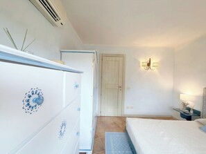A bedroom with a bed, a dresser, a door, and a wall-mounted light fixture. - Mirto Smeraldo by Casa Check (Porto Rotondo)