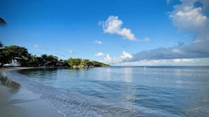 A beach with calm waters, a clear sky, and a small island with vegetation and buildings. - Conch Casitas - King or 2 Singles, AC, Shared Pool (Roatán)