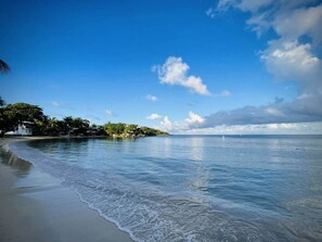 A beach with calm waters, a clear sky, and a small island with vegetation and buildings. - Conch Casitas - King or 2 Singles, AC, Shared Pool (Roatán)