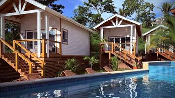 A poolside view of a resort with two wooden cabins, each with a staircase leading to a deck.