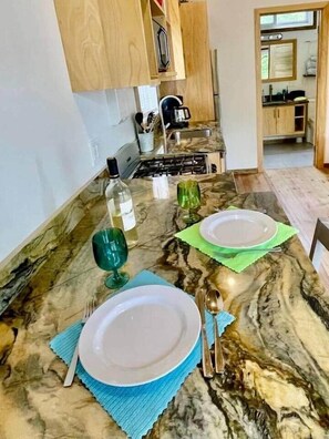 A marble dining table set with plates, cutlery, and glasses, with a kitchen in the background.
