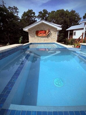 A swimming pool with a stone wall and a sign, surrounded by trees.