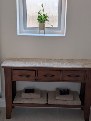 A wooden console table with a tiled countertop, two drawers, and a shelf with two folded towels. - Cambridge Town House (Cambridge)