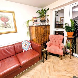 A living room with a red leather sofa, a pink armchair, a wooden cabinet, and various plants. - Cambridge Town House (Cambridge)
