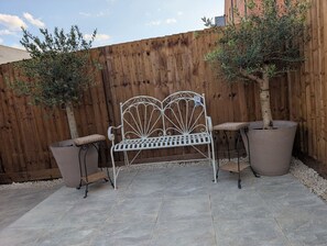 A metal bench with a decorative backrest, flanked by two potted plants with tall, slender trunks. - Cambridge Town House (Cambridge)