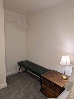 A small room with a bench, a wooden nightstand, a lamp, and a clothing rack. - Cambridge Town House (Cambridge)