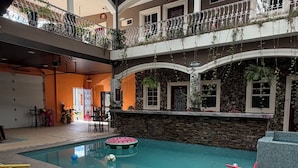 Una piscina interior con pared de piedra, techo con tragaluces y zona de estar con sillas y mesas.
