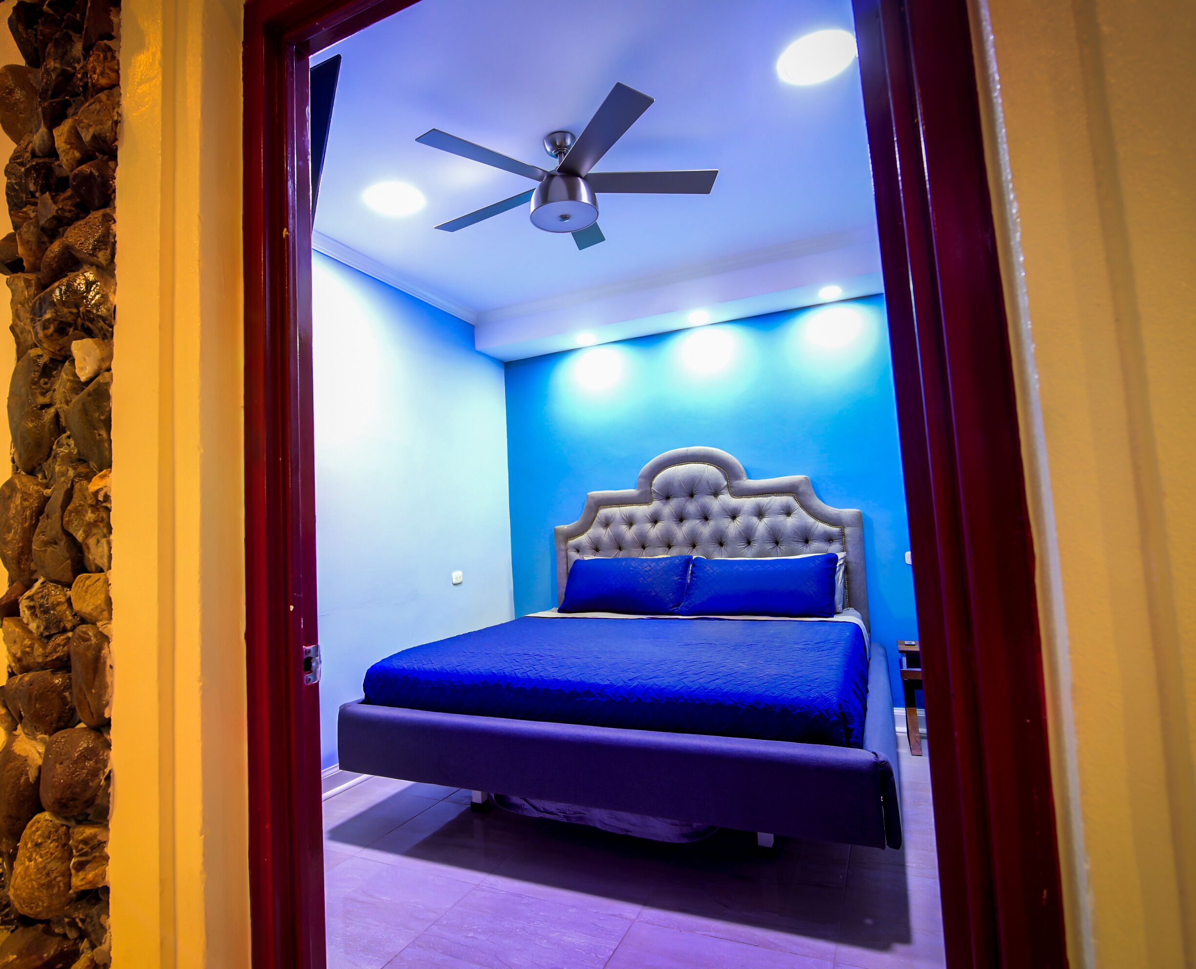 A bedroom with a bed, a ceiling fan, and a stone wall.