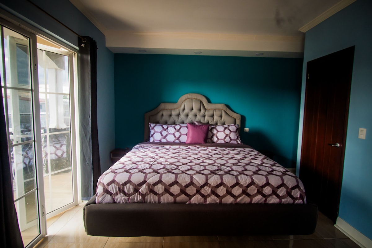 Un dormitorio con una cama grande, una mesita de noche y un ventanal corredera que da a un espacio exterior.